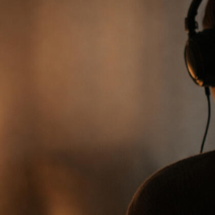 A person sitting in soft light, listening through headphones in a quiet, intimate atmosphere.